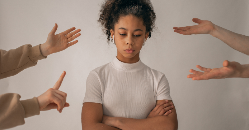 Menina com braços cruzados com dedos sendo apontados a ela