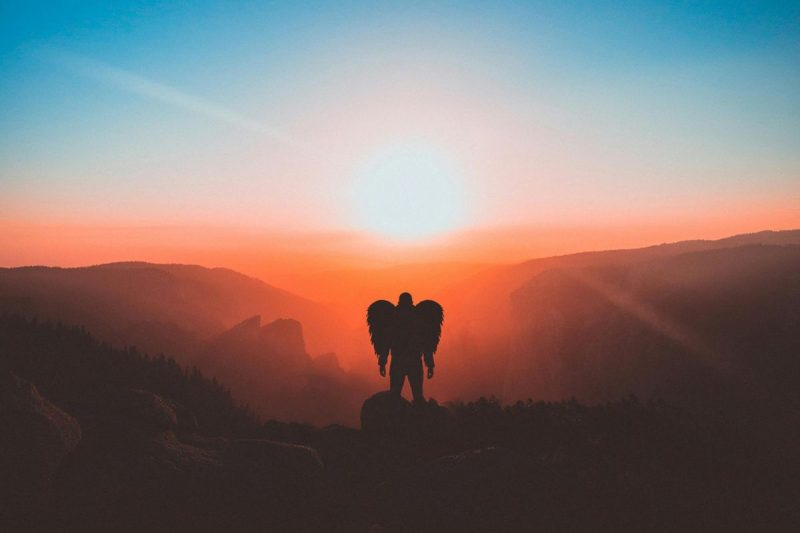 anjo da guarda com as asas abertas em um campo aberto ao ar livre em um lugar alto e com o sol ao fundo