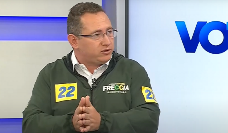 Homem branco usando óculos de grau sentado com casaco verde militar. Ele segura as mãos na altura do abdômen, gesticulando enquanto está com a boca semiaberta. Eduardo Freccia foi o primeiro entrevistado na NDTV