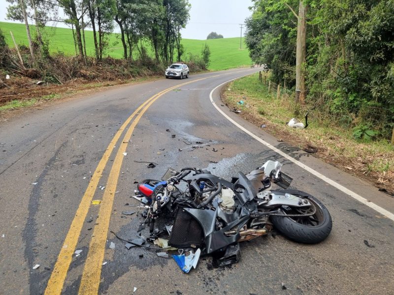 Moto de luxo ficou aos pedaços com a colisão. Imagem mostra motocicleta caída na pista com a carenagem destruída e óleo sob a rodovia. Ao fundo aparece uma viatura da Polícia Militar de Santa Catarina