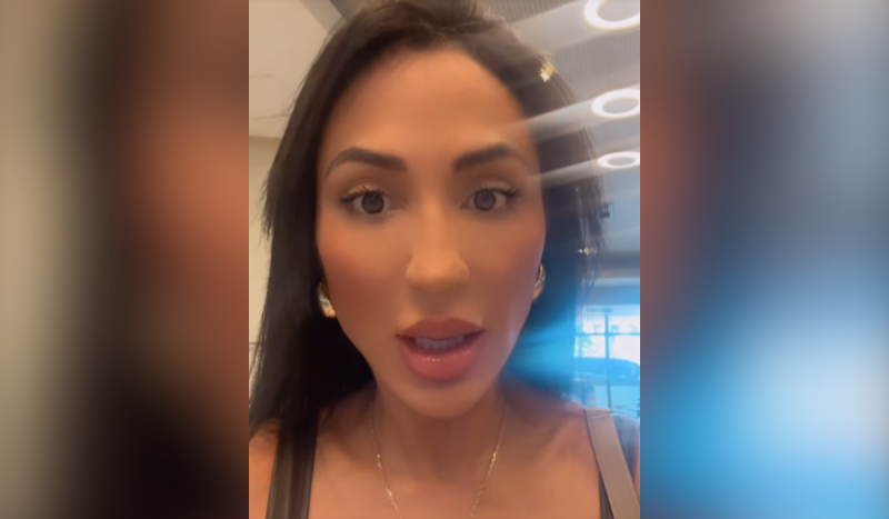 Irmã de Deolane Bezerra - mulher branca com boca aberta enquanto fala. Ela tem cabelos lisos e compridos, usa brincos de argolas grandes douradas e colar fino dourado