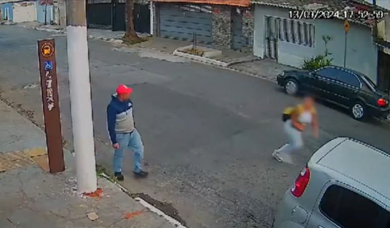 Maníaco da Mooca atacando mulher na rua - foto mostra homem de casaco azul e cinza, usando boné vermelho e calça jeans azul, tentando atacar mulher na rua. As imagens são de câmeras de segurança