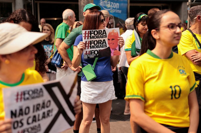 Mulher segura placa com foto do ministro do STF Alexandre de Moraes com o escrito hashtag Fora Moraes