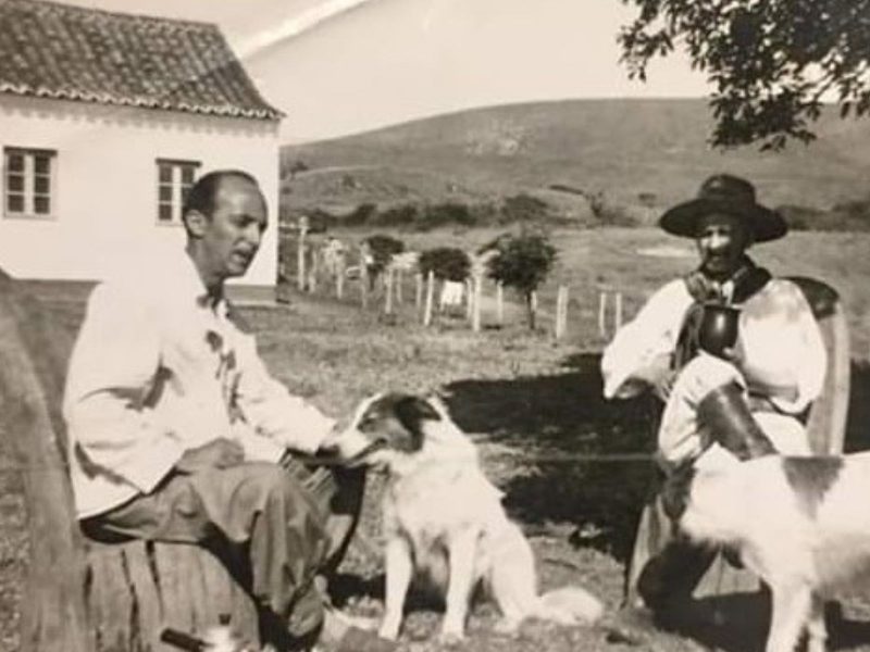 A imagem em preto e branco mostra cachorros da raça ovelheiro gaúcho com colonos gaúchos.