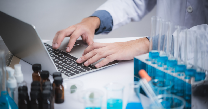 Imagem de pessoa teclando em computador com frascos de tubo de ensaio