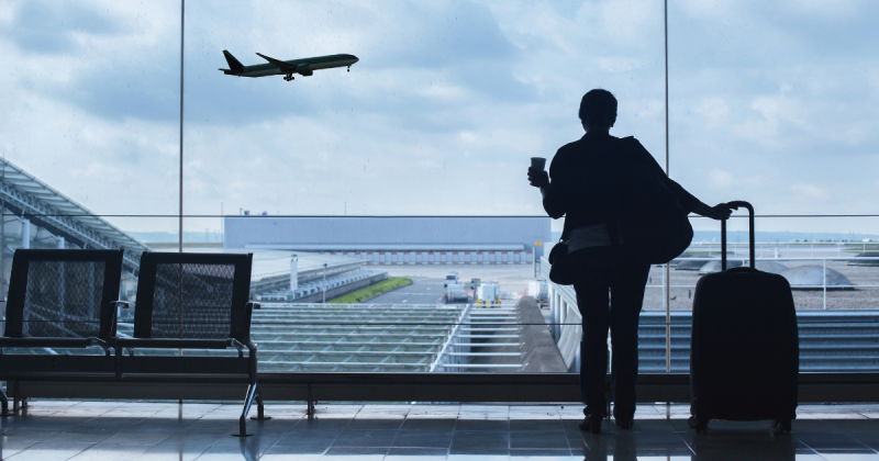 Pessoa com mala em aeroporto vendo avião