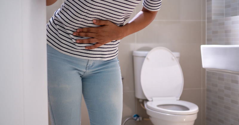 Mulher se apoiando em porta de banheiro com mãos na barriga