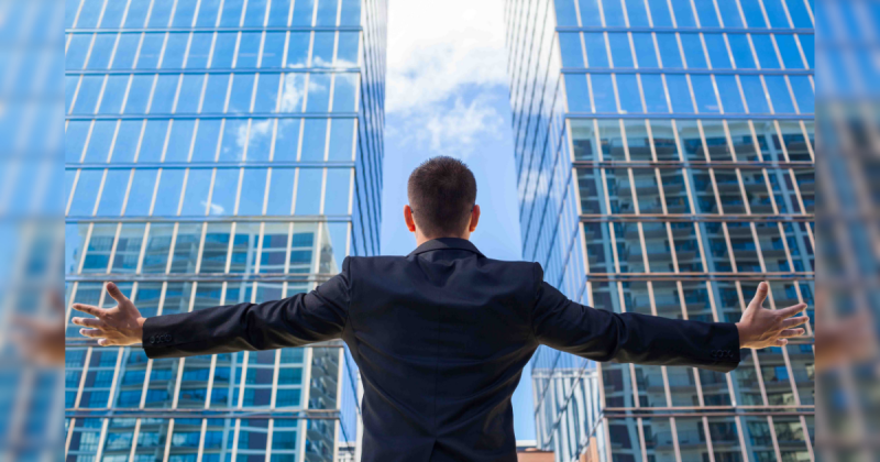 Homem de sucesso em frente a dois prédios com os braços abertos