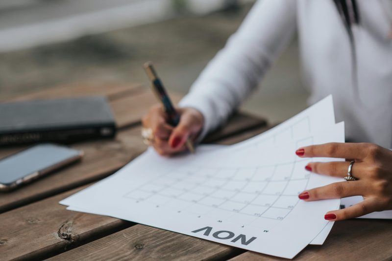 mãos de uma mulher segurando um calendário no mês de novembro e com a mão direita ela escreve no calendário