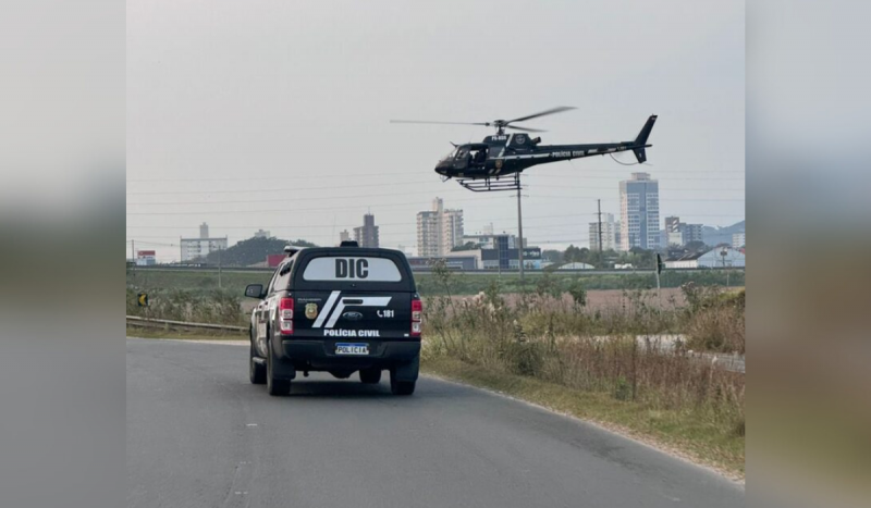 Viatura da polícia civil na cor preta andando na rua enquanto um helicóptero também da Polícia de SC sobrevoa - ações estão investigando facção que atuava em SC