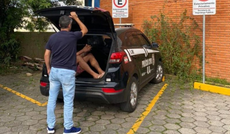 Suspeito de incendiar a moto da ex em Florianópolis é preso, foto mostra ele dentro de porta-malas de viatura da PCSC enquanto policial fecha a porta