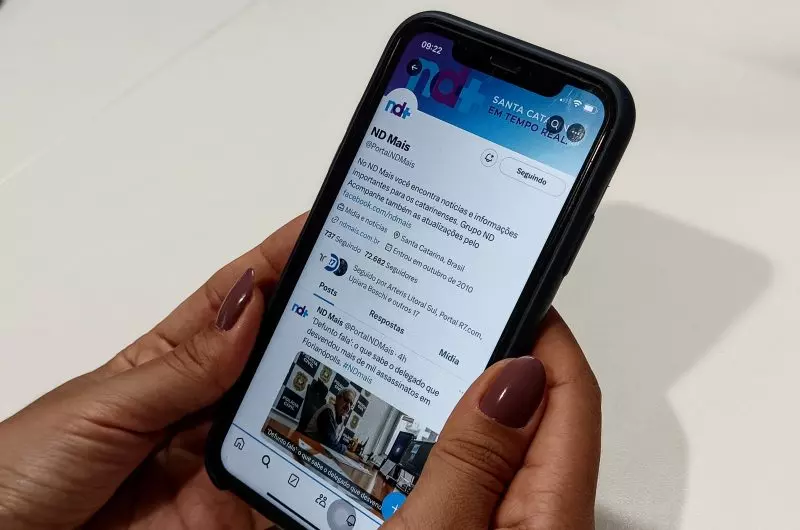 Mãos segurando celular aberto em perfil do portal ND Mais no X (antigo twitter)