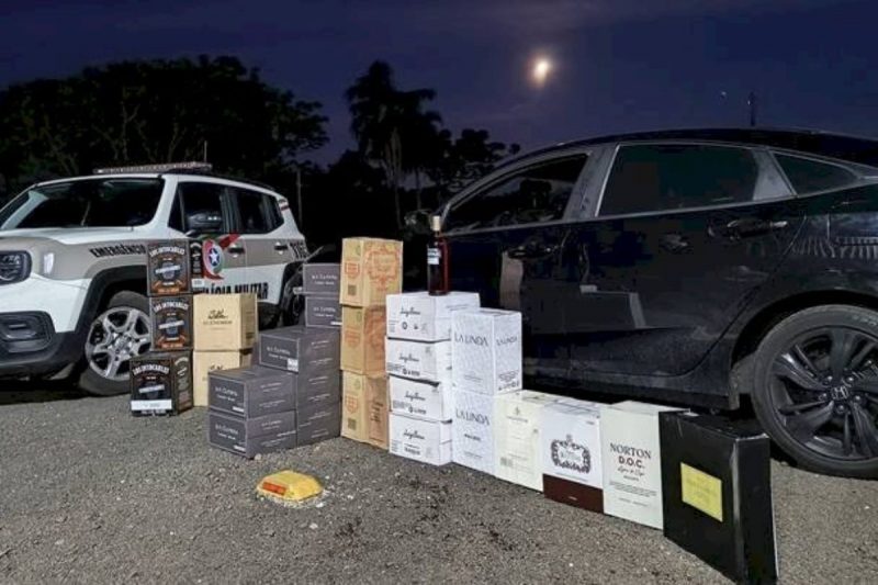 32 caixas de vinho argentino empilhadas na frente do carro honda/civic e ao lado da viatura da pm