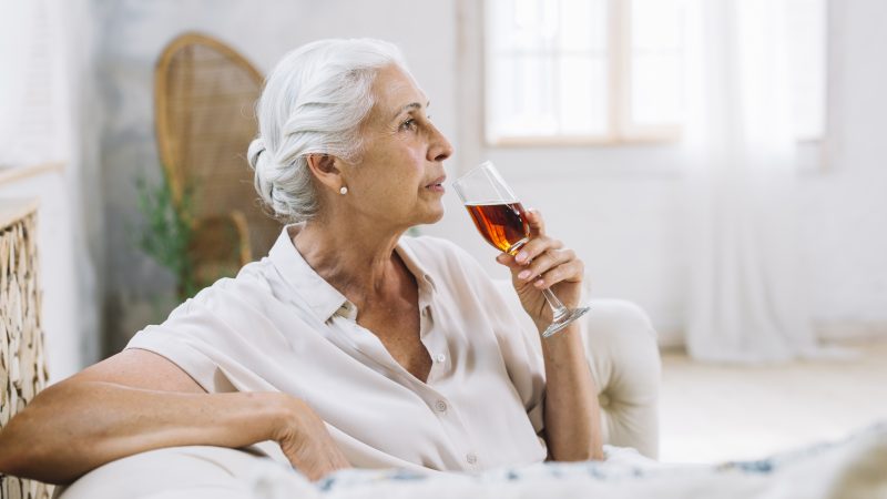 Mulher idosa bebendo um vinho em seu sofá