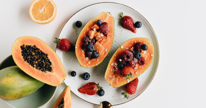 Mamão, com frutas vermelhas dentro deles e laranjas