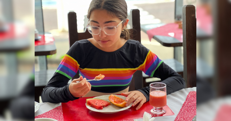 Menina em mesa comendo mamão e melancia ao mesmo tempo