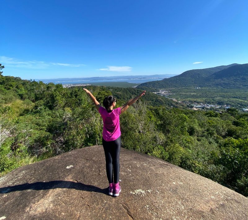 Mulher, de braços abertos, em uma pedra no Morro do Lampião, uma das trilhas de Florianópolis