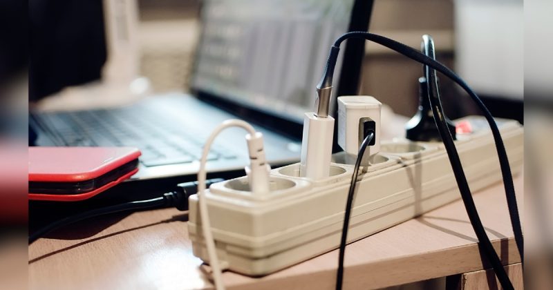 Extensões e réguas de energia em cima de mesa com computador e celular