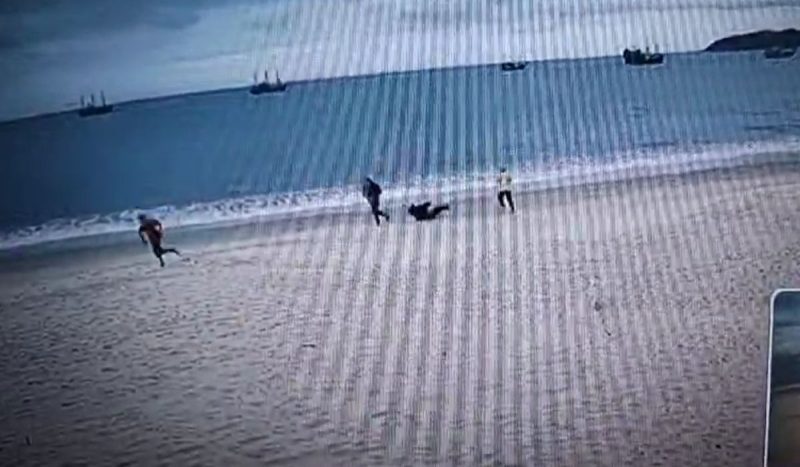 Assalto em praia de Florianópolis terminou com mulher caída na areia - vídeo de câmera de segurança mostra duas pessoas correndo enquanto uma está caída na areia de praia e uma outra vê a cena