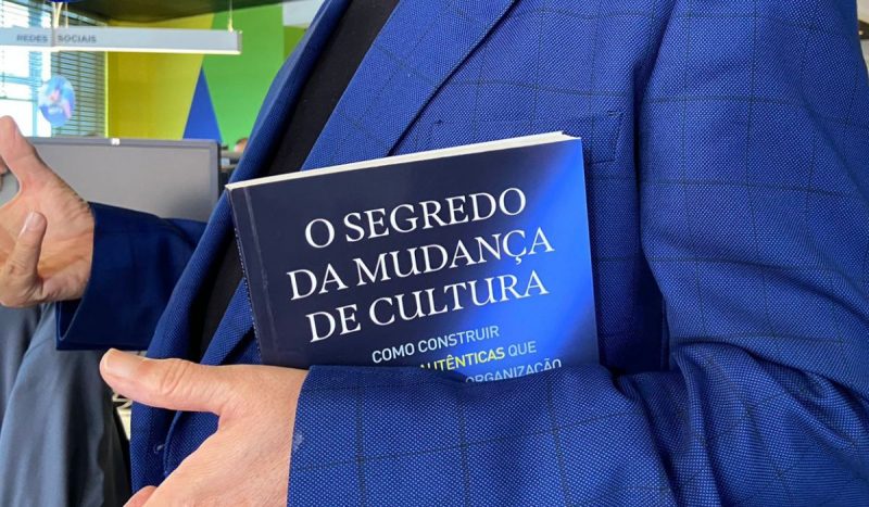 Destaque em braços de homem idoso segurando livro de capa azul e preto entre um dos braços 