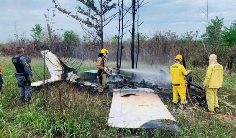 Bombeiros usando trajes amarelos apagando fogo de aeronave que está queimando no chão