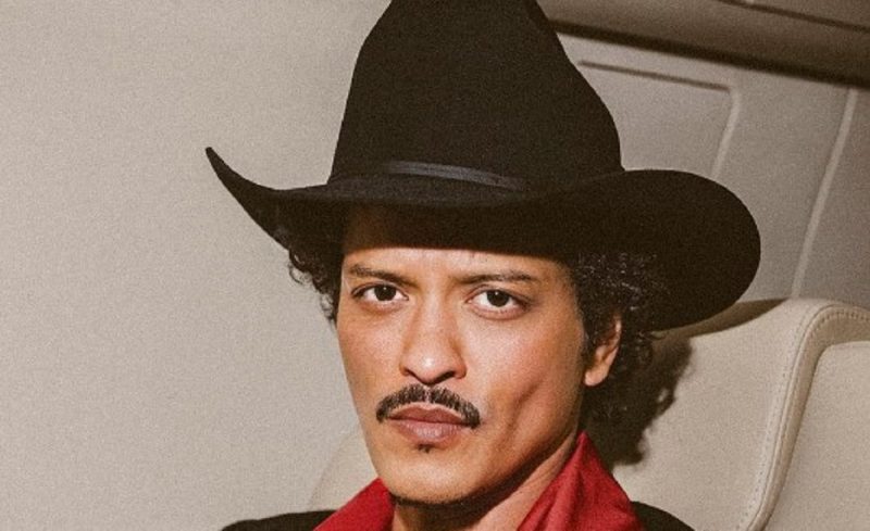 na foto aparece Bruno Mars de chapéu em carro indo para o show