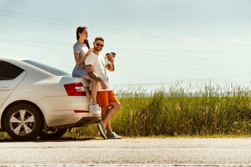 Casal curtindo feriado encostado na traseiro de um carro estacionado no campo