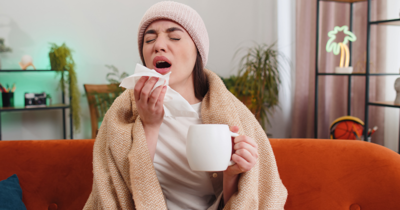 Pessoa doente com toca e lençol por cima tomando chá de gengibre e açafrão