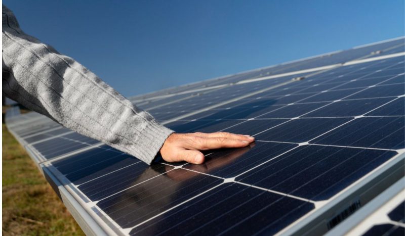 A imagem mostra uma mão tocando uma placa de energia solar.