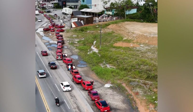 Distribuição de gasolina grátis em SC - fila de carros vermelhos vista de cima por drone