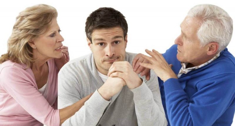 Homem no meio da mãe e do pai com rosto de frustração para ilustrar a interferência dos pais no relacionamento