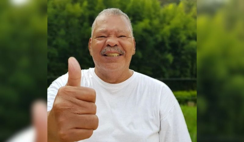 Maguila morreu após ETC - homem negro, gordo, usando camiseta branca básica, sorrindo e fazendo joinha com o dedo