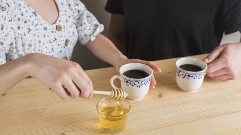 Mulher adoçando o café com mel 