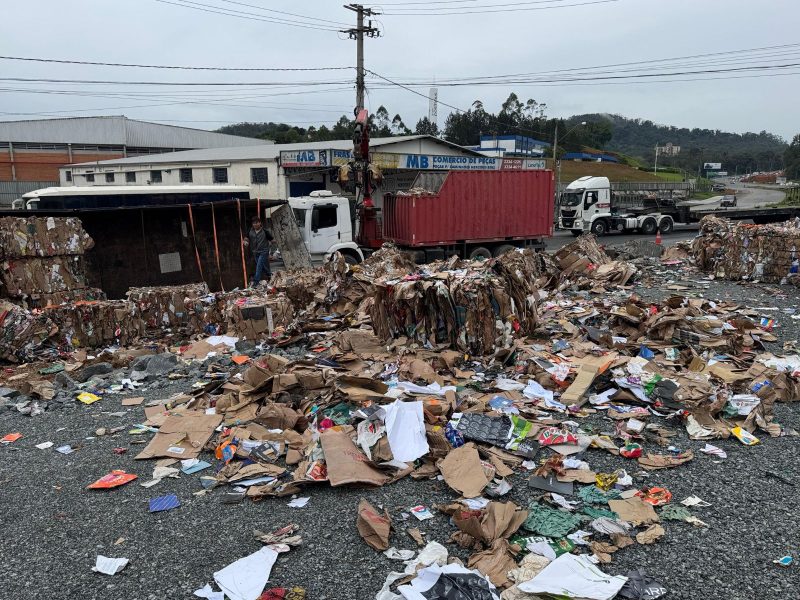 A imagem mostra um caminhão tombado e a carga derramada no chão.