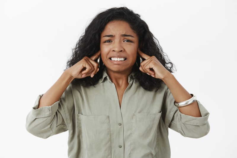 mulher negra fazendo cara de desconforto com os dedos tampando os ouvidos