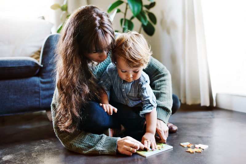 mãe brincando de quebra-cabeça com o filho no chão 