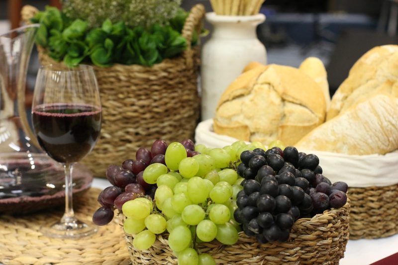 Mesa com cesta de pães e uvas, acompanhada de taça de vinho 