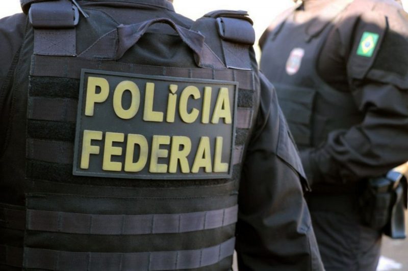 A imagem mostra um policial com o colete da Polícia Federal.