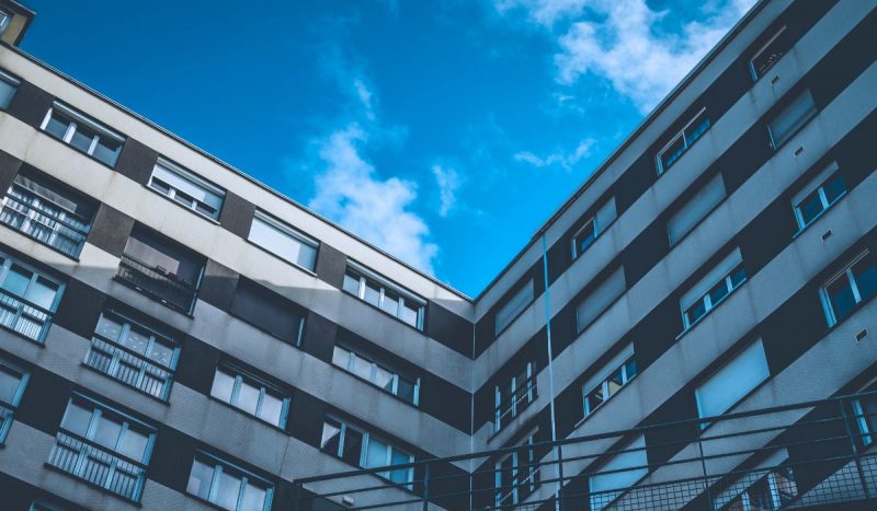 foto mostra janelas de prédio cinza com fundo de céu azul com nuvens para falar sobre preço médio de aluguel para apartamentos de um quarto