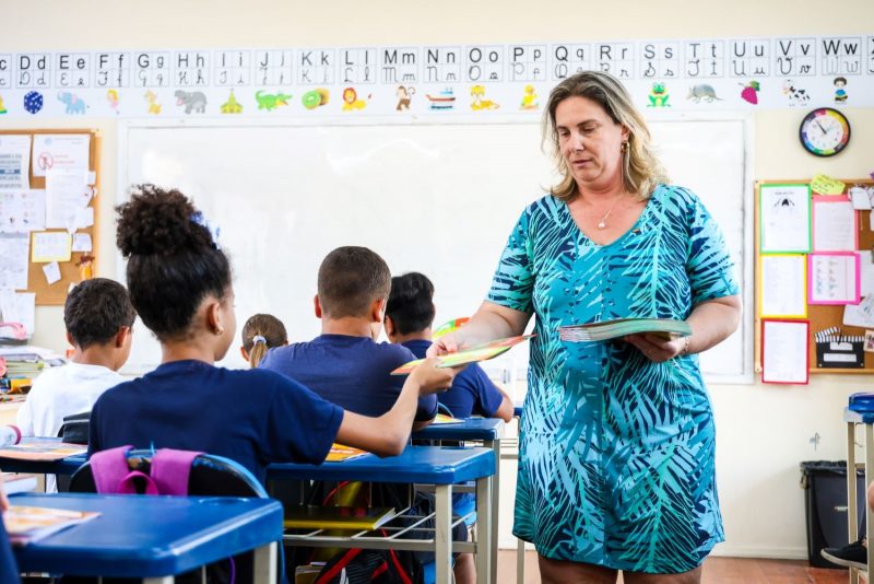 Professora distribuindo material em sala de aula