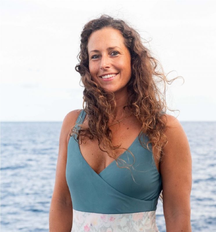 Foto de Giulia em uma praia, com os cabelos ao vento e o mar ao fundo 