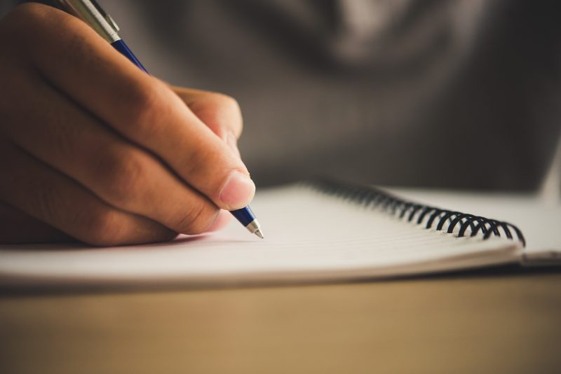 Homem escrevendo em um caderno com uma caneta