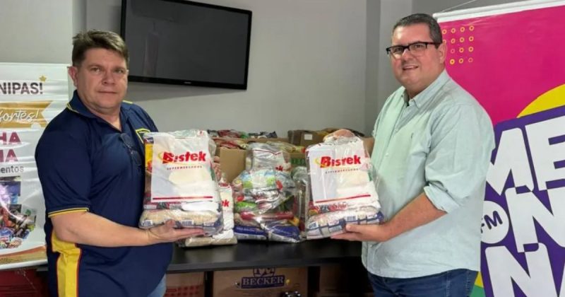 Dois homens segurando sacos de alimentos em campanha de arrecadação da Rádio Menina