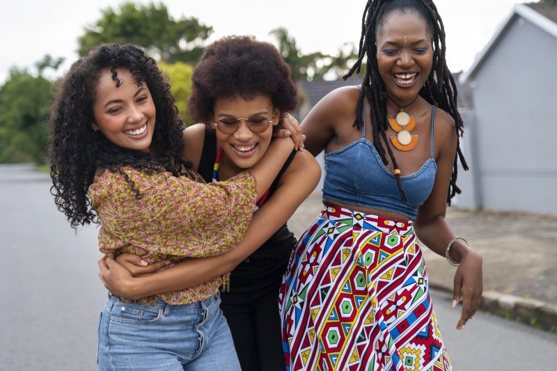 Tres mulheres negras se abraçando e sorrindo enquanto caminham na rua 