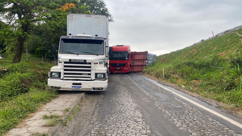 A imagem mostra uma carreta tombada e um caminhão atolado.