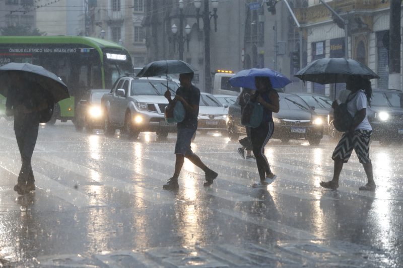 Pessoas atravessando a rua com sombrinhas embaixo de forte chuva