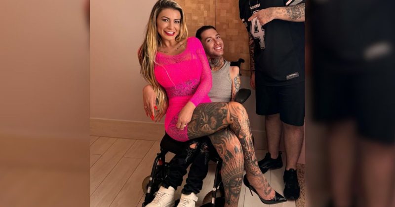 Andressa Urach em colo de homem sentado em cadeira de rodas