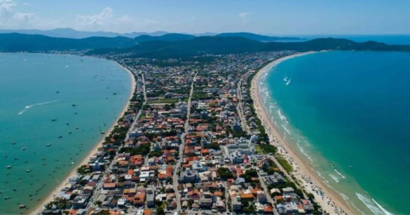 Imagem aérea de Bombinhas, com uma faixa de terra cercada pelo mar azul e límpido de ambos os lados