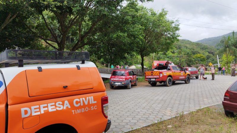 A imagem mostra carros de Bombeiros e Defesa Civil que buscam pela criança levada pela correnteza.