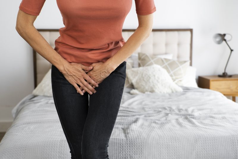 Mulher com as mãos na frente da região íntima, como o corpo retorcido em desconforto